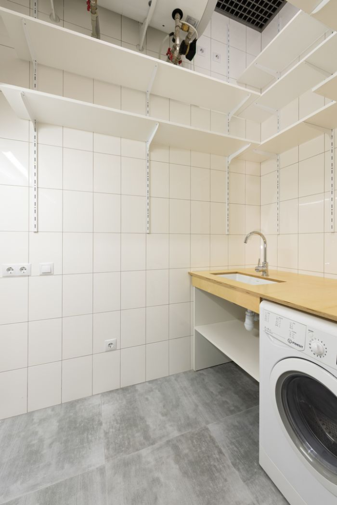 Spacious laundry room featuring a washer, sink, and ample shelving in a minimalist design.